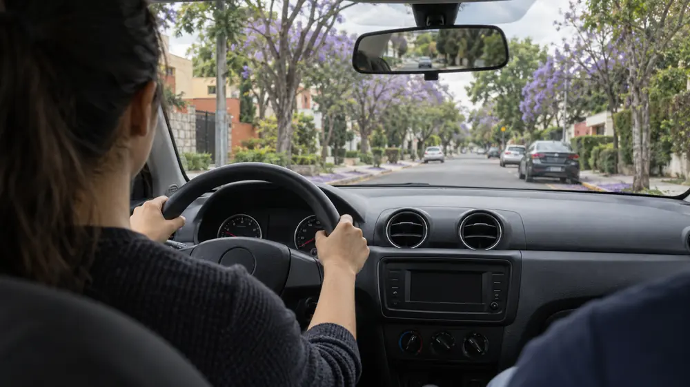 Alumno al volante durante una clase de manejo en una calle arbolada con jacarandas de la Ciudad de México