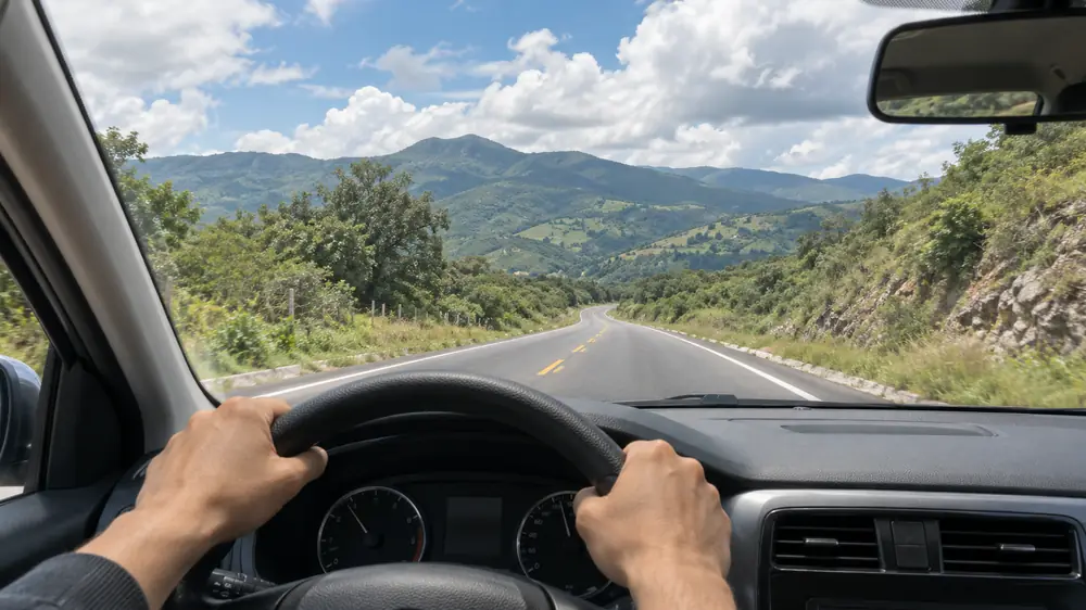 Carretera de dos carriles con cerros vista desde un auto de práctica en una clase de manejo en carretera